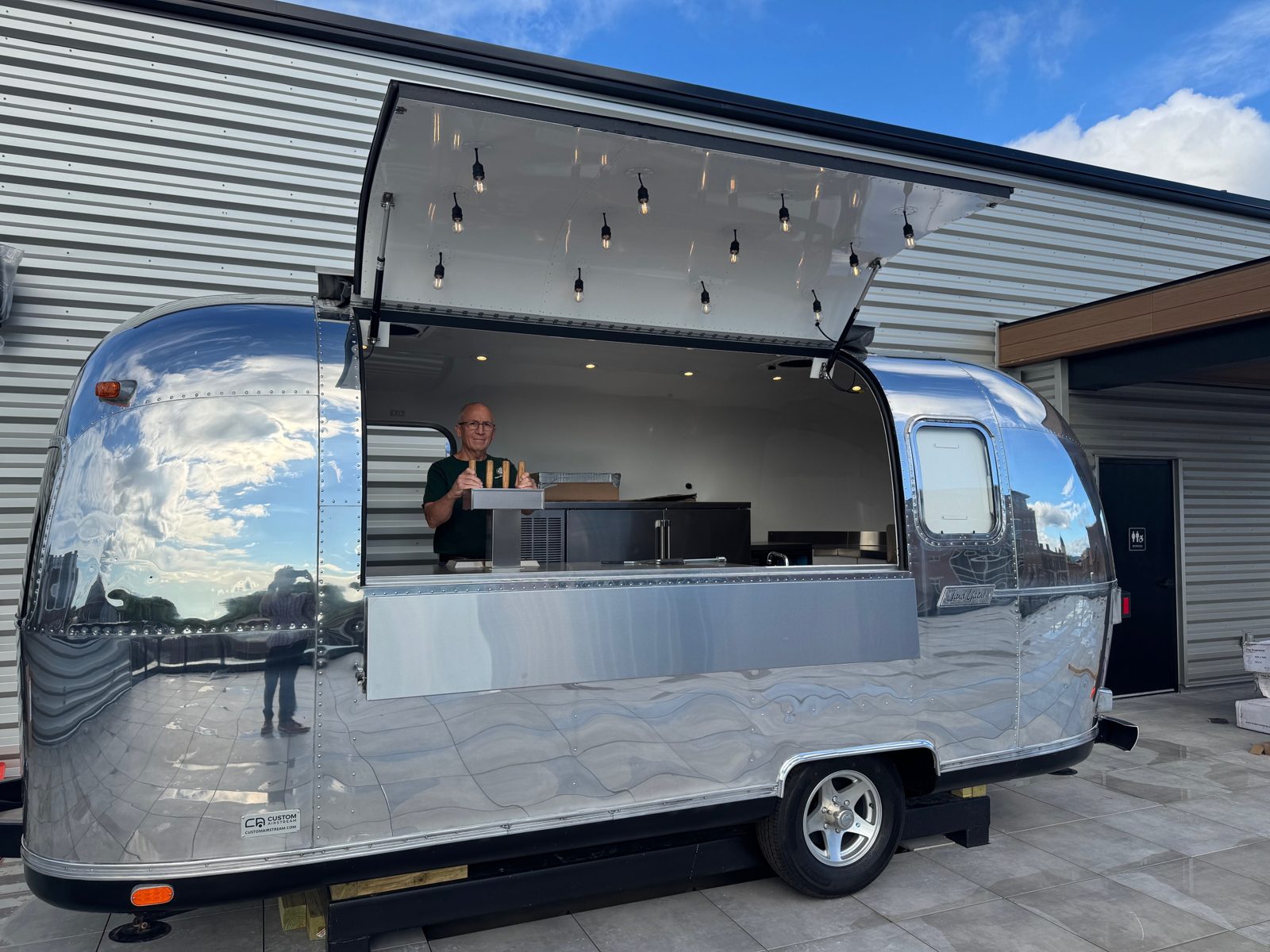 Polished Airstream food trailer with pendant string lights under the open service awning