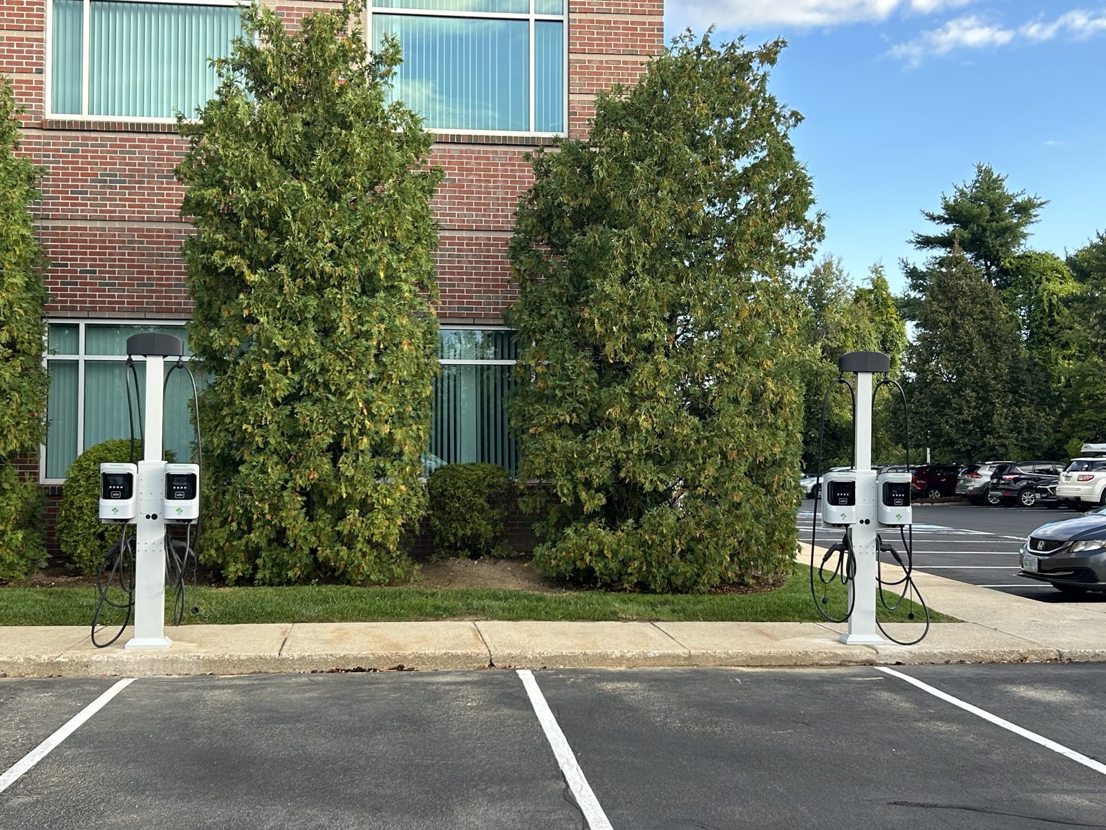 Two dual port Level 2 EV charging pedestals installed at the edge of a commercial parking lot in New Hampshire
