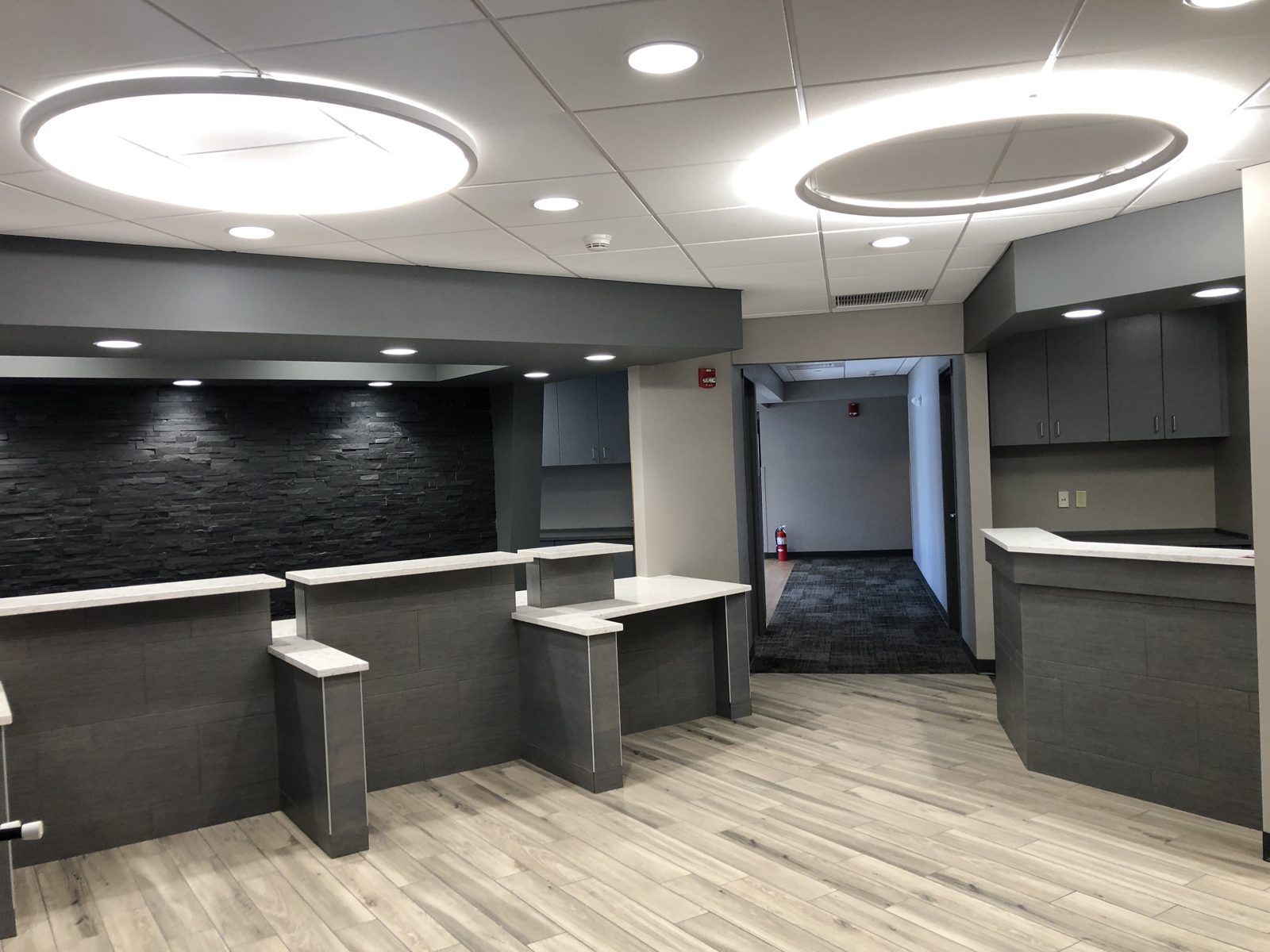 Reception area with two large LED ring fixtures, recessed downlights and a stone feature wall
