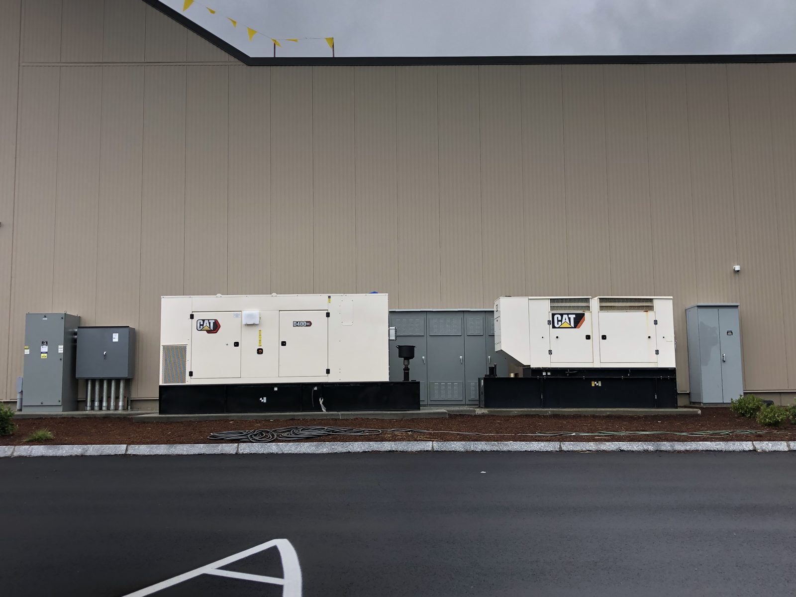 Two enclosed standby generators and transfer equipment along the wall of an industrial building in New Hampshire