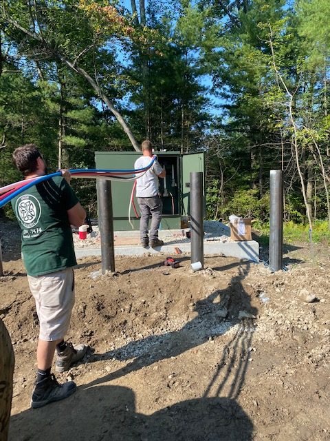 Two Irish Electric electricians pulling cable into a pad mount cabinet on a wooded site in New Hampshire