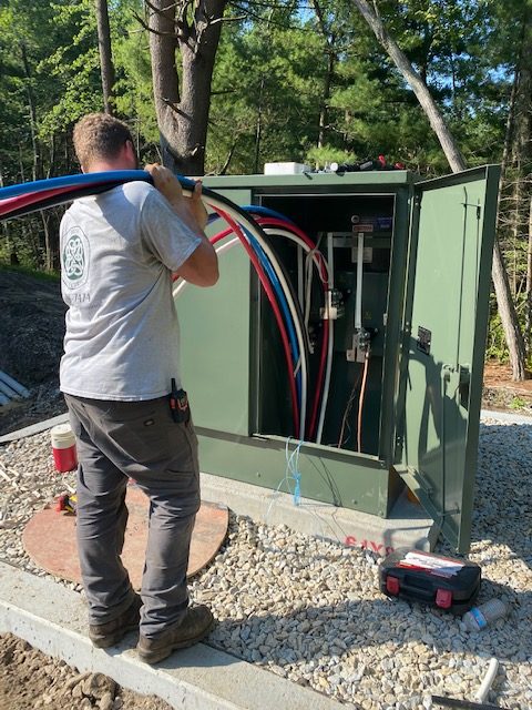 Electrician feeding red, white and blue conductors into a green pad mount cabinet