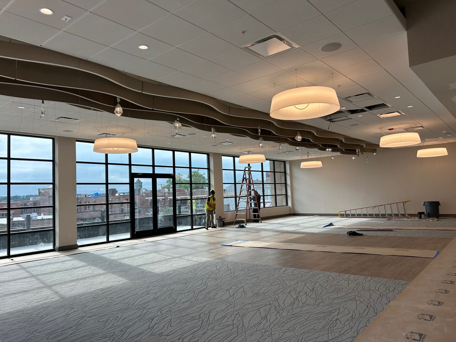 Electricians finishing pendant lighting in a large event hall with floor to ceiling windows, New Hampshire