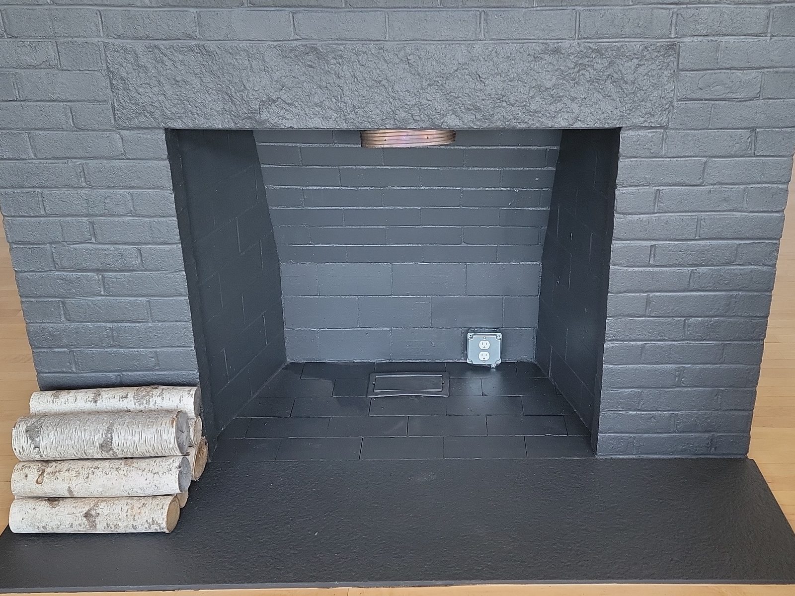 Painted brick fireplace with a receptacle mounted on the inside wall of the firebox and birch logs on the hearth