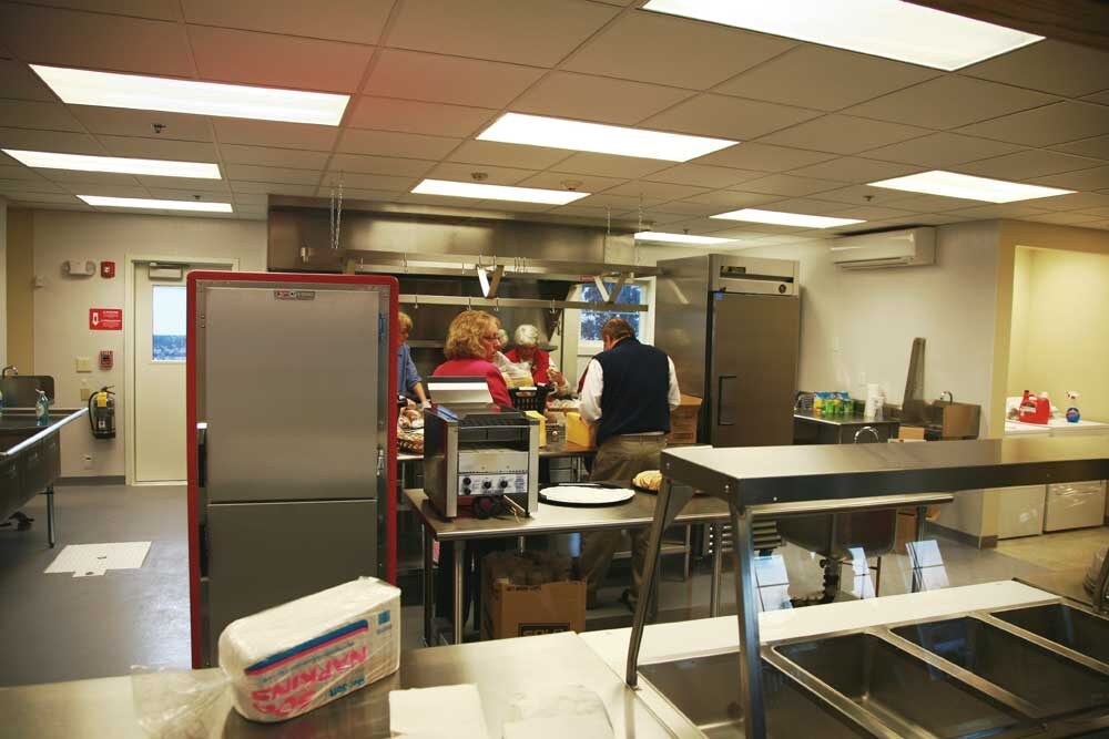 Finished commercial kitchen and servery at The Friendly Kitchen in Concord, New Hampshire, lit by recessed troffer lighting above stainless steel counters