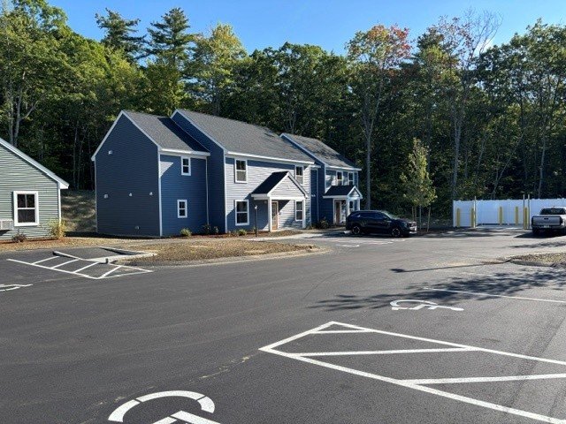 Blue townhouse buildings around a marked asphalt parking area bordered by trees