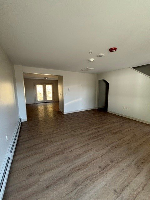 Empty room with wood-look flooring, white walls and an open hallway