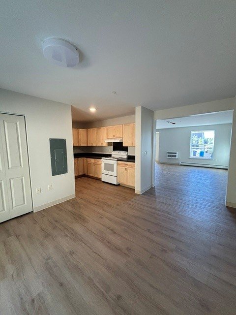 Open kitchen and living area with wood-look flooring, cabinets, stove and windows
