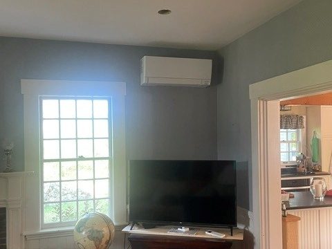 Ductless mini split indoor unit mounted high in the corner of a living room beside a window