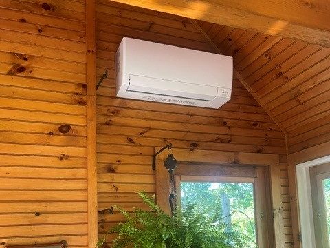 Ductless mini split indoor unit mounted high on a knotty pine wall under a sloped wood ceiling