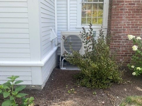 Mini split outdoor unit on a stand beside a brick chimney and white clapboard siding