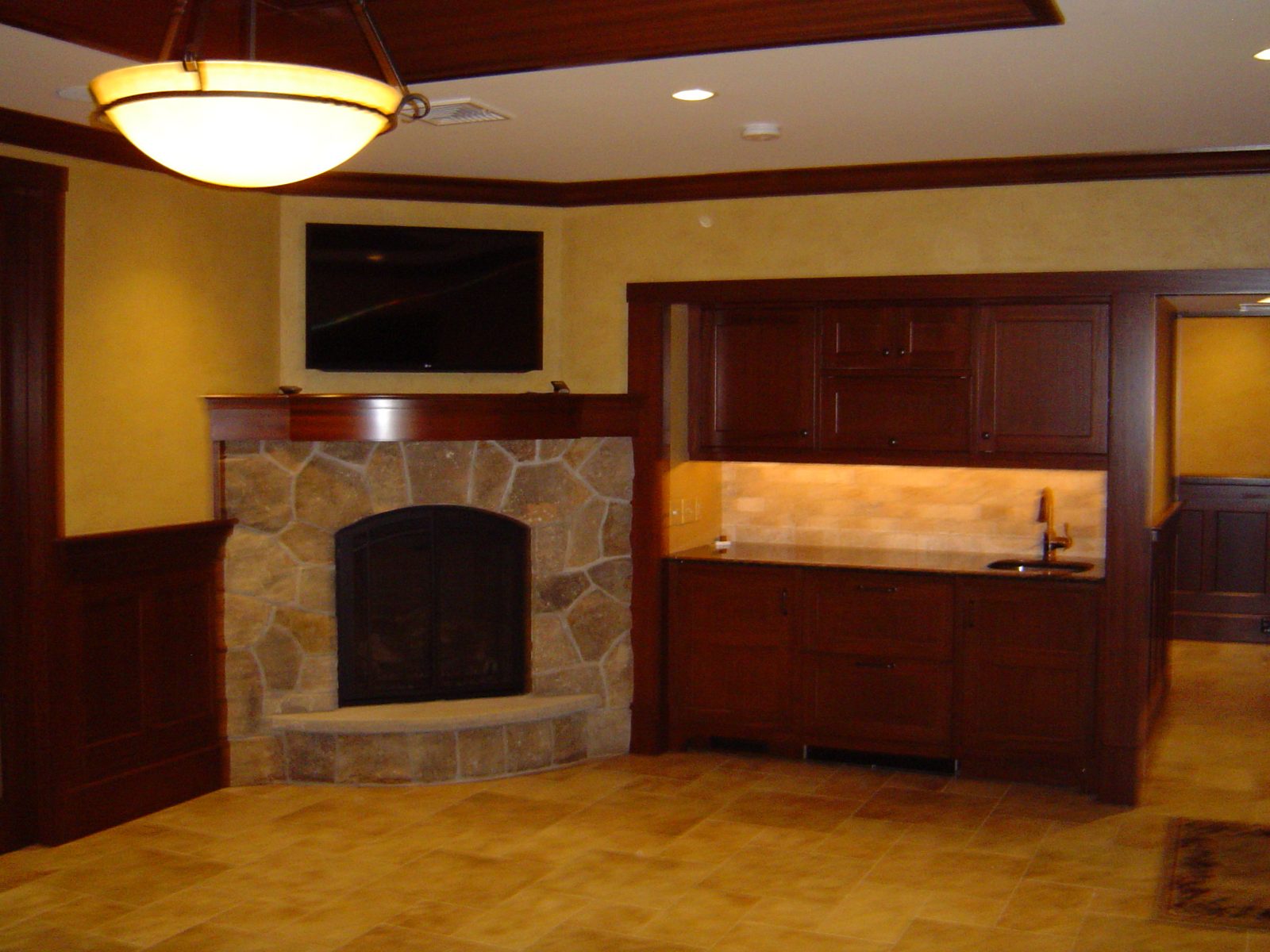 Lounge with stone fireplace, wet bar with under cabinet lighting and a pendant fixture