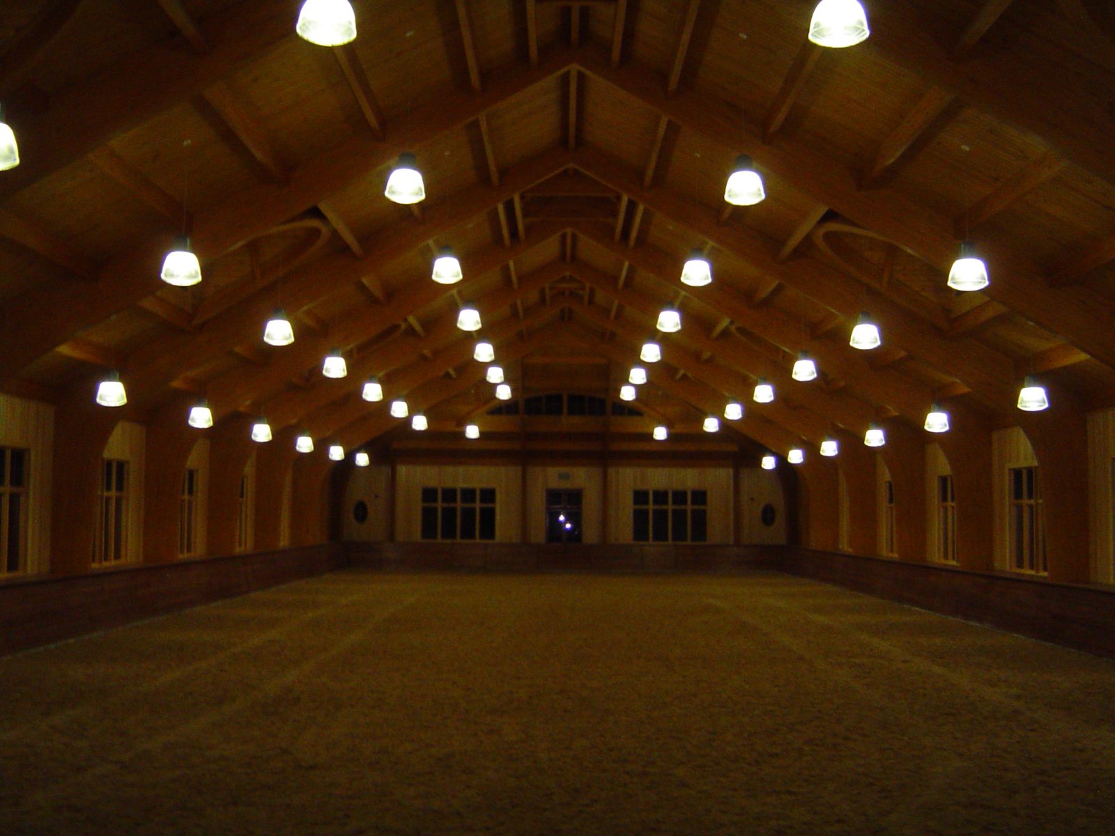 Indoor riding arena with rows of pendant high bay lights under a timber roof