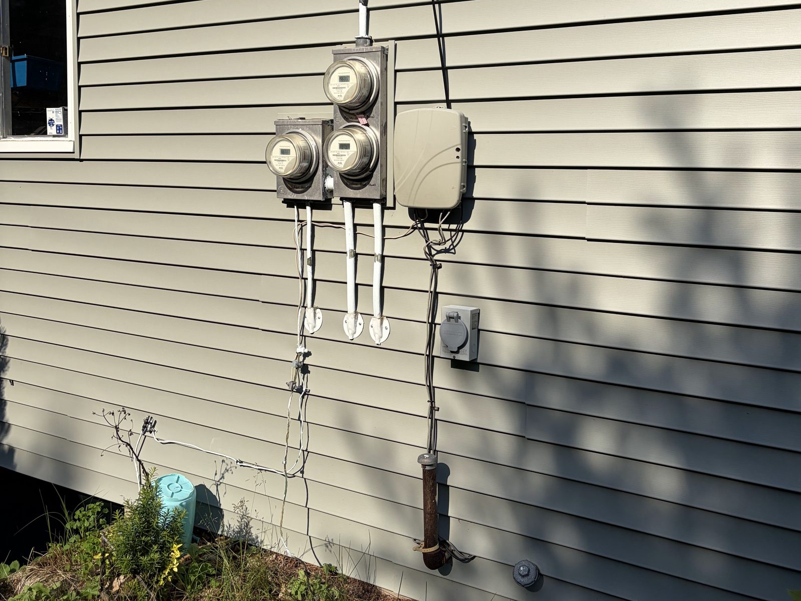 Three older meter sockets, two stacked and one single, on the vinyl-sided wall of a house before a service change