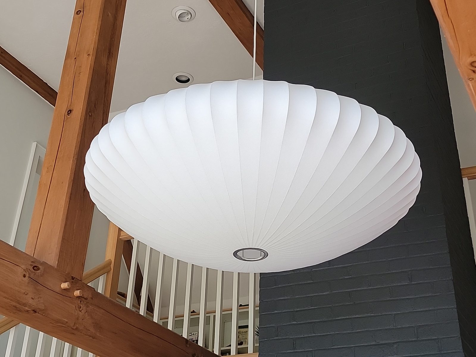 Large white round pendant light hung from a vaulted timber frame ceiling beside a painted brick chimney